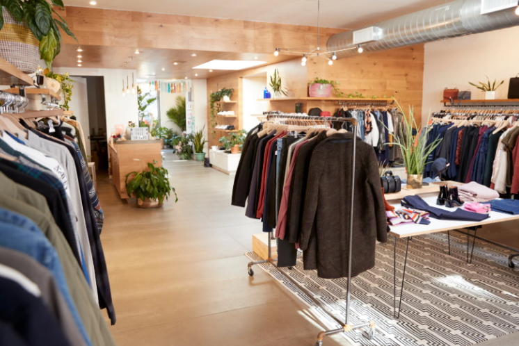 Bright, modern clothing boutique with neatly arranged racks of garments, plants and accessories displayed on shelves and tables.