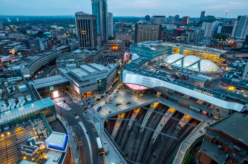 Aerial view of Birmingham city centre at dusk, showing Grand Central station, railway tracks and surrounding modern office buildings.