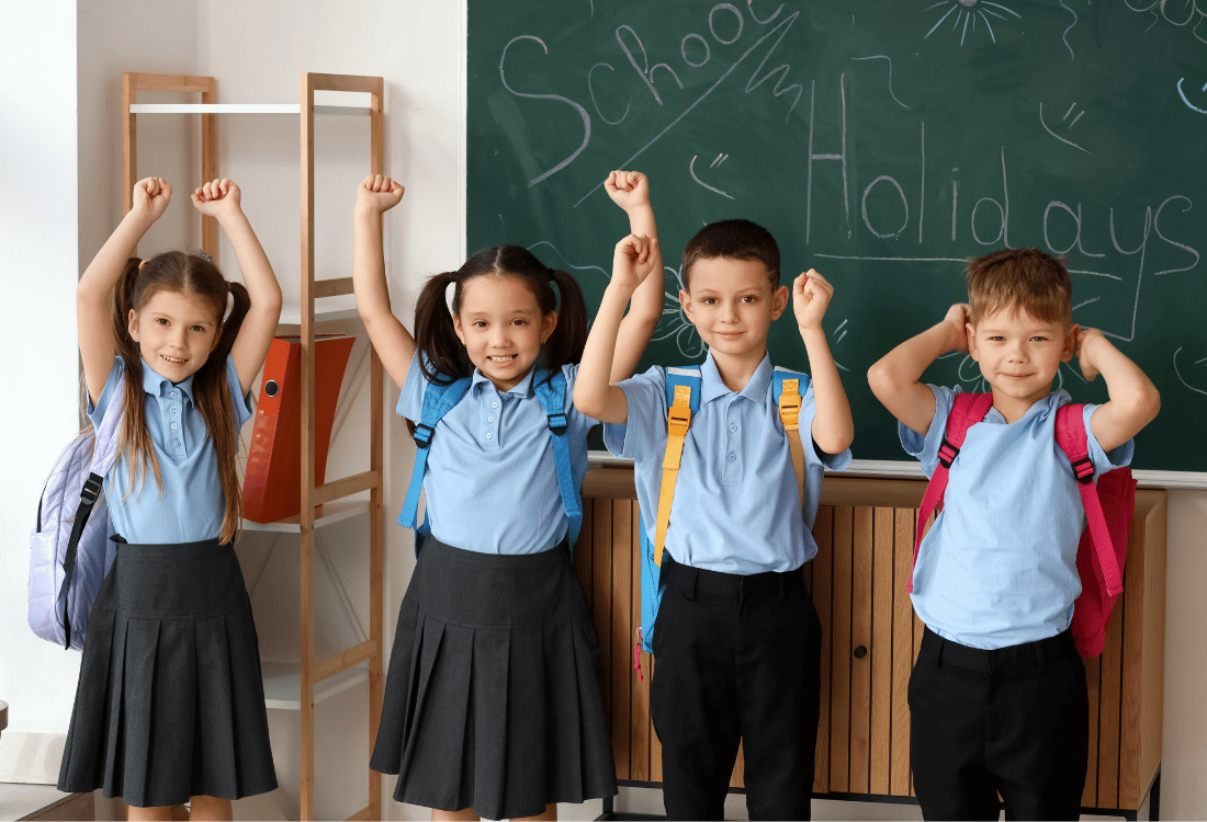 Four schoolchildren in uniform stand in front of a chalkboard with 